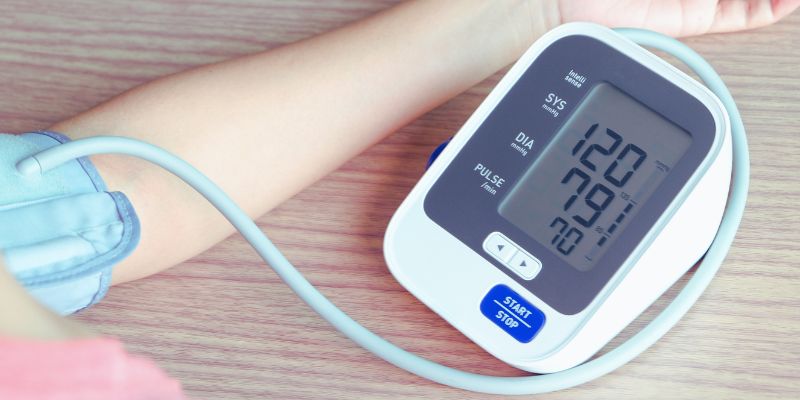 A close-up of an arm with a blood pressure cuff, connected to a digital monitor displaying readings of 120/79 for blood pressure and a pulse rate of 70. 