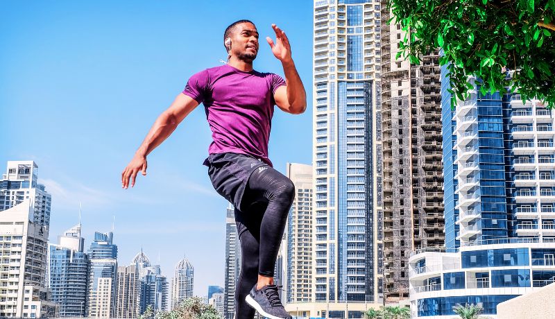 A man in a purple athletic shirt and black workout pants running outdoors,