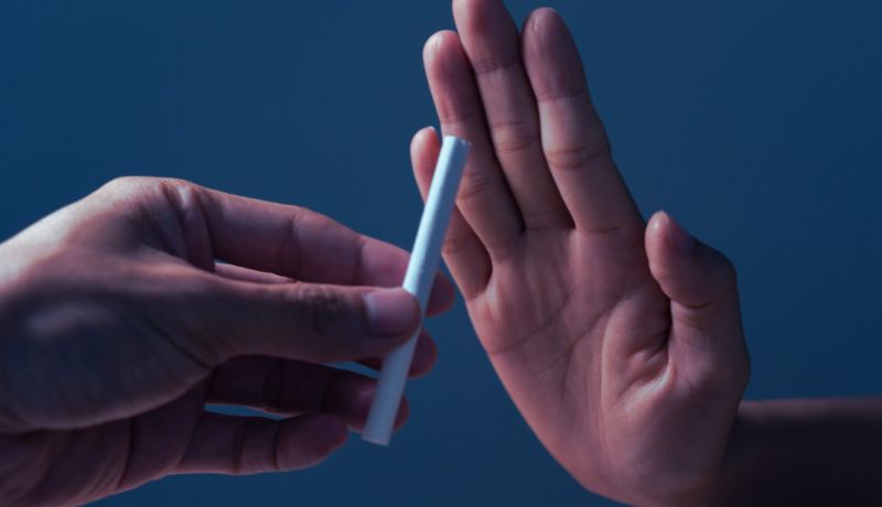 A close-up image showing one hand offering a cigarette while the other hand is raised in a gesture of refusal