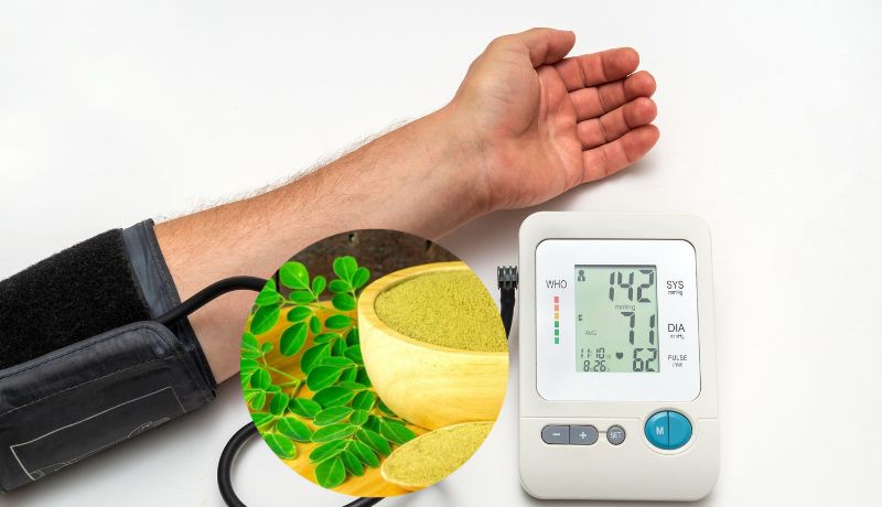 A person's arm with a blood pressure cuff attached, connected to a digital blood pressure monitor, and an inset image of moringa powder and leaves.